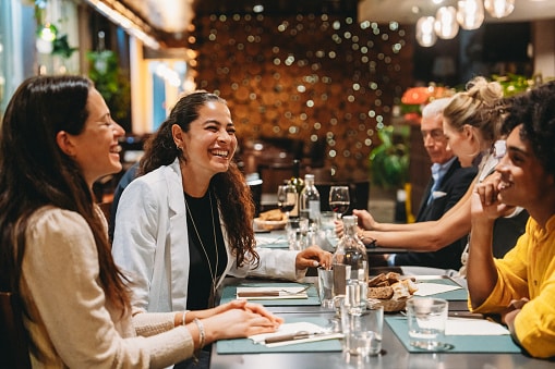 Group of friends laughing and enjoying dinner together at a restaurant, celebrating and having fun